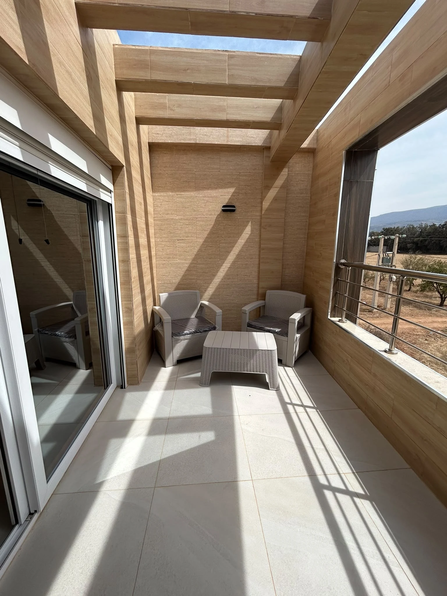 Terrasse privative en bois abritée par une pergola avec salon extérieur et vue sur les reliefs de Nedroma
